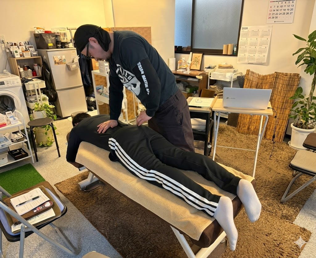 徒手療法大学神戸校の実技授業で、指導者がうつ伏せになった学生の腰部から骨盤にかけて触診と徒手アプローチを指導している様子